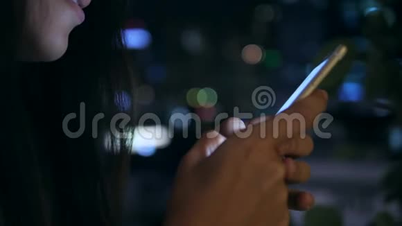 迷人的年轻女孩使用智能手机与模糊的蓝色波克街城市夜灯背景4K曼谷视频的预览图