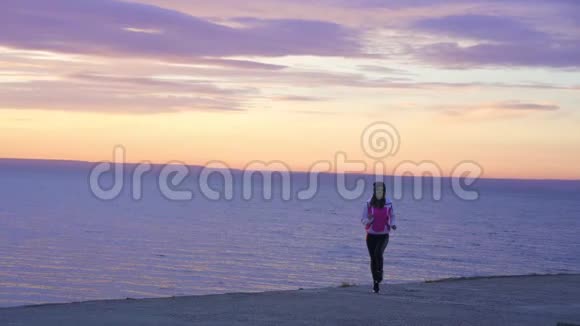 慢动作年轻苗条的女孩戴着运动帽和运动夹克早上在大河堤上慢跑视频的预览图