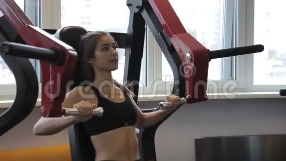 年轻女子在现代健身房室内做坐式胸压机视频的预览图