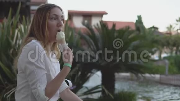 棕榈树背景下美丽积极的年轻女性吃冰淇淋的肖像视频的预览图