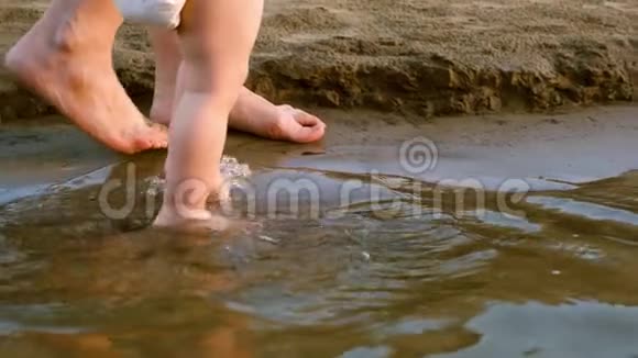 婴儿穿着尿布沿着河岸走第一步洒上水和母亲一起散步腿慢慢视频的预览图