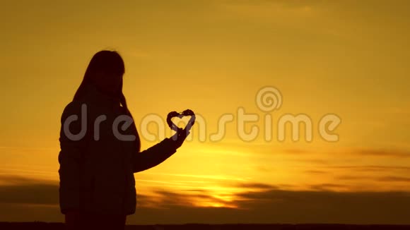 一个女孩在美丽的日落和明亮的太阳上抱着一颗心的孤独剪影视频的预览图