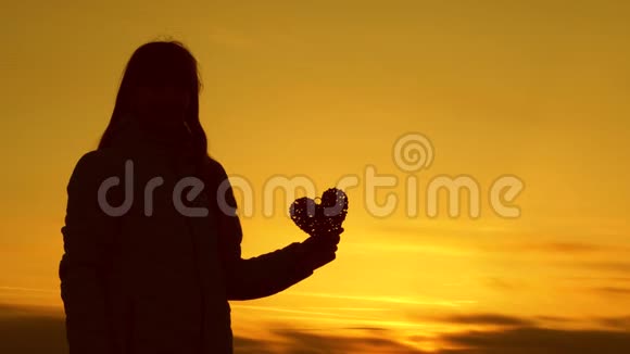 一个女孩在美丽的日落和明亮的太阳上抱着一颗心的孤独剪影视频的预览图