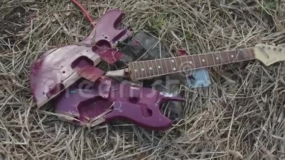 关闭破碎的紫色吉他躺在枯萎的干草上俯视库存破电吉他部件紫罗兰甲板视频的预览图