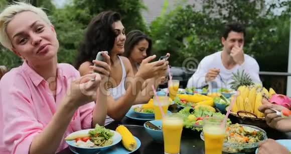 人们集体谈论吃健康的素食食品朋友们使用手机智能手机坐在热带露台上视频的预览图