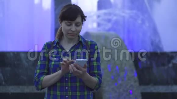 晚上女人在喷泉旁边使用白色智能手机视频的预览图