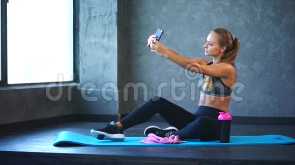 一个身材好的年轻女孩在健身房的手机上自拍视频的预览图