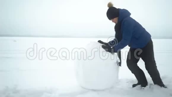 男孩在冬天为雪人滚动大雪球视频的预览图