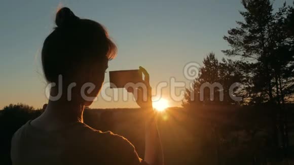 女子剪影拍照惊人日落与智能手机在公园视频的预览图