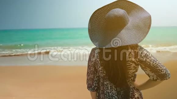海滩上的女孩戴着蓝色的帽子和蓝色的裙子看着海洋近距离射击慢动作视频的预览图