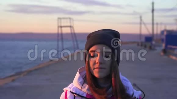 慢动作年轻苗条的女孩戴着运动帽和运动夹克早上在大河堤上慢跑视频的预览图
