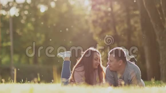 夏日绿茵上的浪漫情侣他们躺在肚子上腿向上他们互相对视着他们视频的预览图