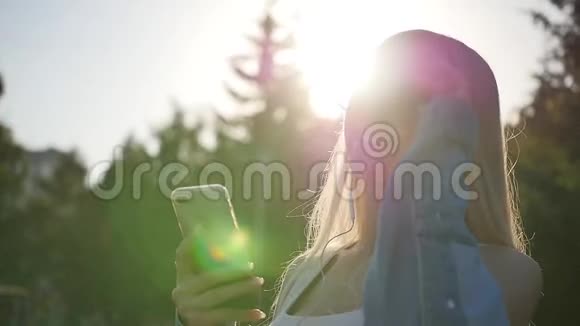 迷人的金发女郎在她的智能手机户外窒息音乐日落时欣赏音乐的女人慢动作视频的预览图