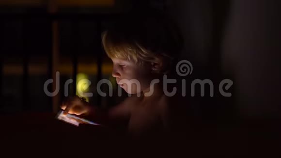小男孩坐在黑暗的房间里玩平板电脑视频的预览图