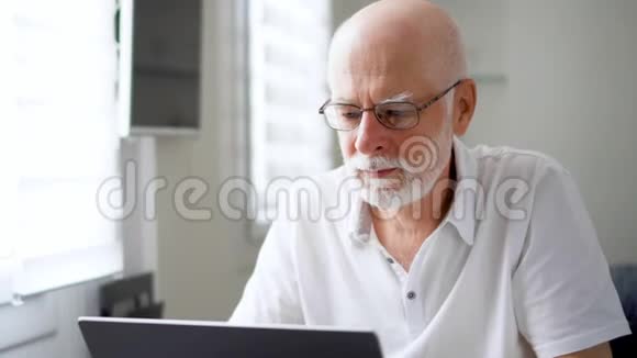穿着劳累过度穿着白色衣服的老人在家里用笔记本电脑工作揉揉他疼痛的眼睛视频的预览图
