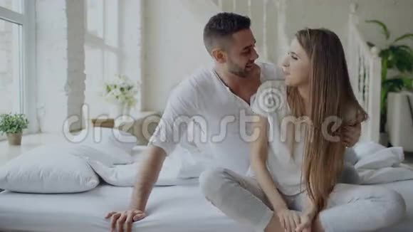 年轻的美丽而有爱心的一对夫妇在早上醒来后坐在床上拥抱和亲吻视频的预览图