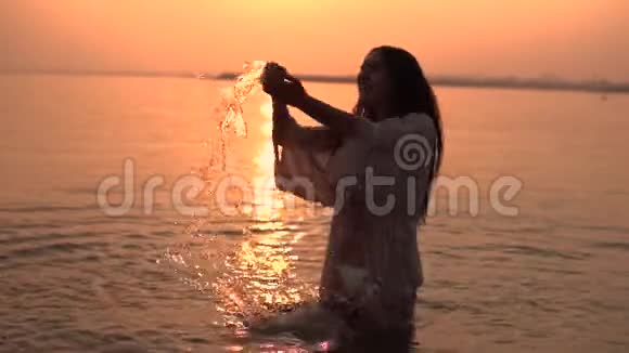 美丽的女孩在阳光的背景下站在水中做溅手慢动作视频的预览图