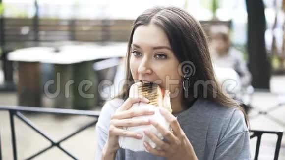 一个年轻漂亮的女人在户外咖啡馆吃一个大三明治视频的预览图