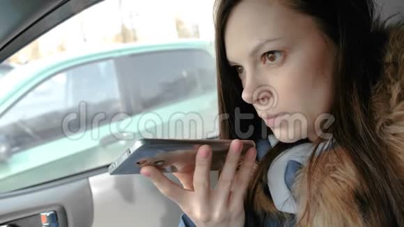 年轻漂亮的女人坐在车里的手机上说着语音信息视频的预览图
