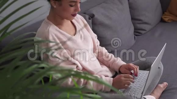 快乐的年轻女子在舒适的沙发上工作手提电脑视频的预览图