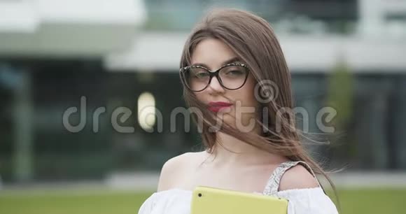 一位戴着眼镜的年轻美女在城市街道的室外看着摄像机的画像视频的预览图