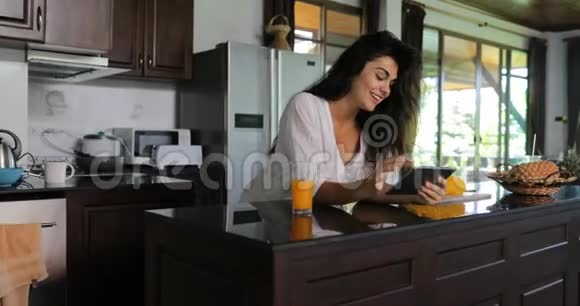 女孩用平板电脑喝果汁笑年轻女子在厨房工作室现代室内视频的预览图