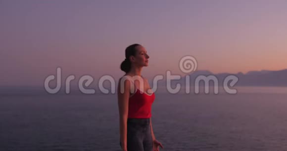 穿红色衣服的白人妇女在日落时在海边的悬崖上练习瑜伽放松身心视频的预览图