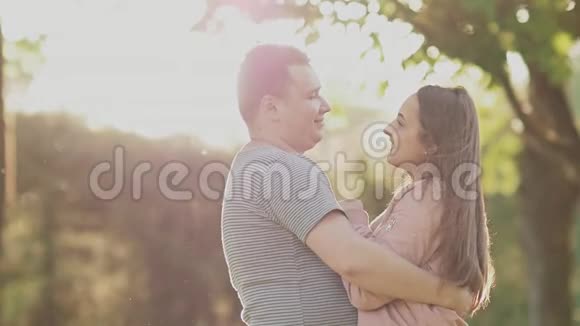一对浪漫的情侣在绿色的夏天公园里男友怀里的女孩一起快乐在阳光下旋转视频的预览图