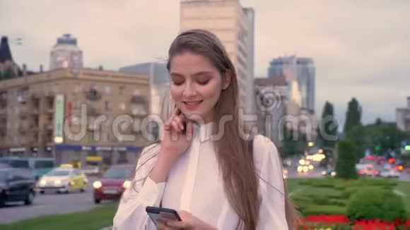 年轻快乐的女孩正在夏季市中心日落时分的智能手机上输入信息这是一种沟通观念视频的预览图