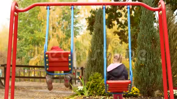 两个孩子骑在秋千上秋天的公园和孩子们用秋千操场视频的预览图