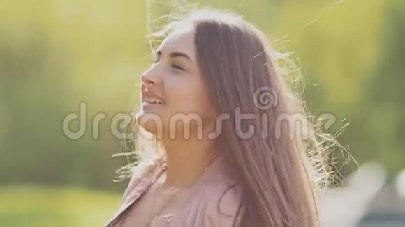 迷人的年轻女孩在公园里摆姿势快乐地旋转这个女孩有一头漂亮的长发特写镜头视频的预览图
