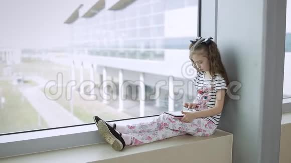 在机场窗口附近的孩子在平板电脑上玩游戏等待飞行时间视频的预览图