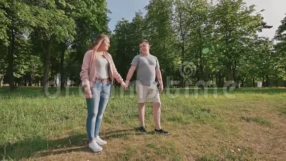 一对浪漫的情侣在绿色的夏天公园里他们牵着手在阳光下奔跑一起快乐视频的预览图