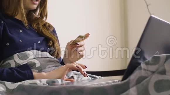 漂亮的快乐女孩坐在床上用信用卡上网购物视频的预览图