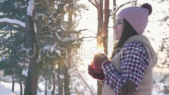 冬天穿着冬衣的女孩在日落时喝着热覆盖的酒在冬天的森林里慢悠悠地视频的预览图