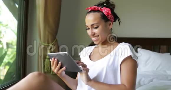 年轻女性使用平板电脑在大窗户上与热带花园美景在线聊天视频的预览图
