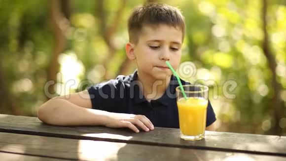 一个男孩在大自然的一张桌子上喝橙汁一个小男孩在户外喝橙汁视频的预览图
