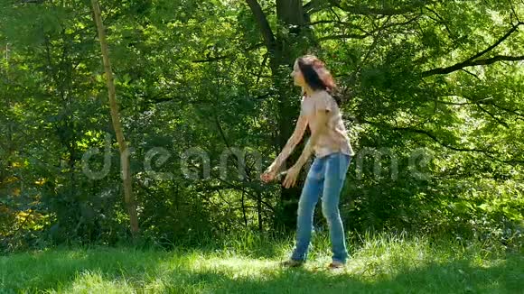 在阳光明媚的温暖日子里穿着粉色衬衫和牛仔裤的快乐迷人的母亲在公园里抱起她的小女儿视频的预览图