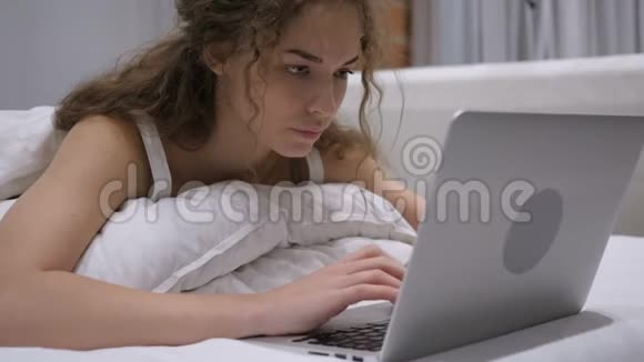 头痛在床上用笔记本电脑工作的女性工作量视频的预览图