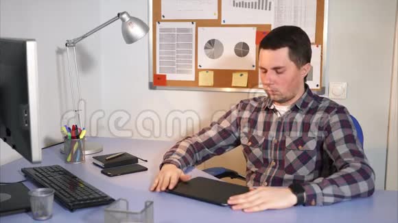 头痛的男人坐在工作场所的后面桌子上放着许多装置视频的预览图