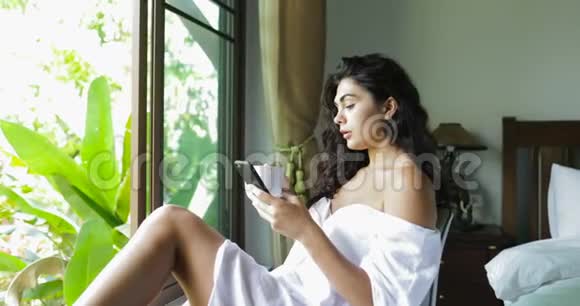 年轻女性使用手机饮料咖啡快乐美丽的女孩在热带大窗户上在线聊天视频的预览图
