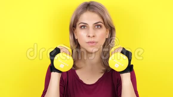 女人在黄色背景下用哑铃练习运动视频的预览图