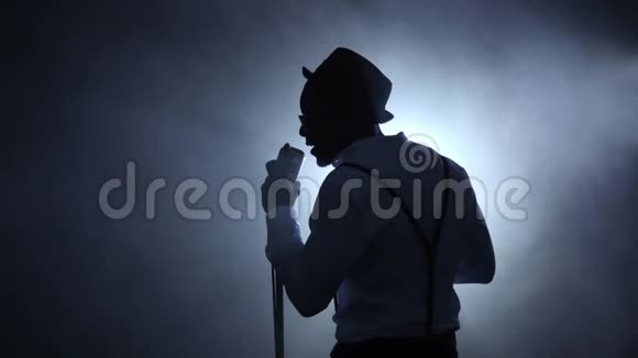 音乐家的视线从后面的烟雾中对着麦克风唱歌黑色背景剪影慢动作视频的预览图