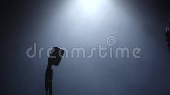 歌手在烟雾和白光中接近麦克风唱歌黑色背景剪影慢动作关门视频的预览图