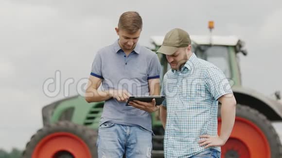 青年农民田间地头交流使用平板在农业机械的背景下视频的预览图