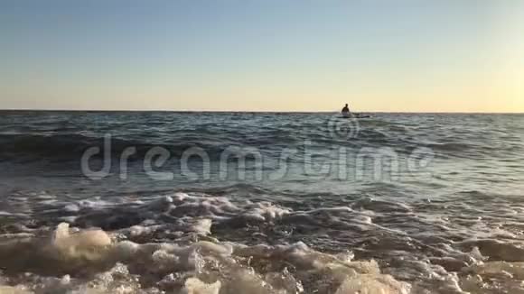 日落时分运动员站在冲浪板上划桨的侧影视频的预览图
