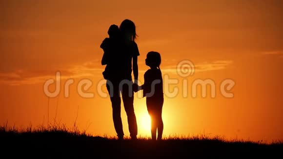 母亲和两个孩子在日落时剪影友好家庭观念视频的预览图