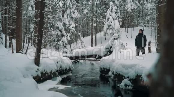 冬天一个旅行者在森林里的河边走在雪覆盖的小径上视频的预览图