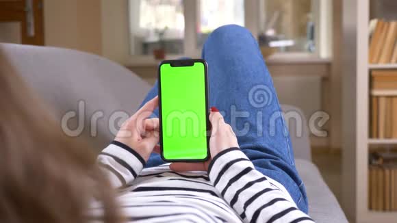 在一个舒适的公寓里用绿色屏幕躺在沙发上的手机拍摄女性特写后景视频的预览图