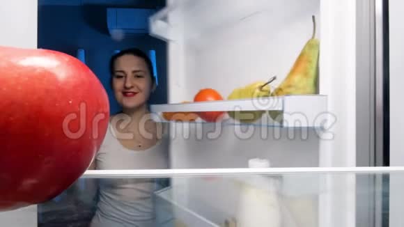 4k视频美丽的微笑女人从冰箱里拿红苹果视频的预览图